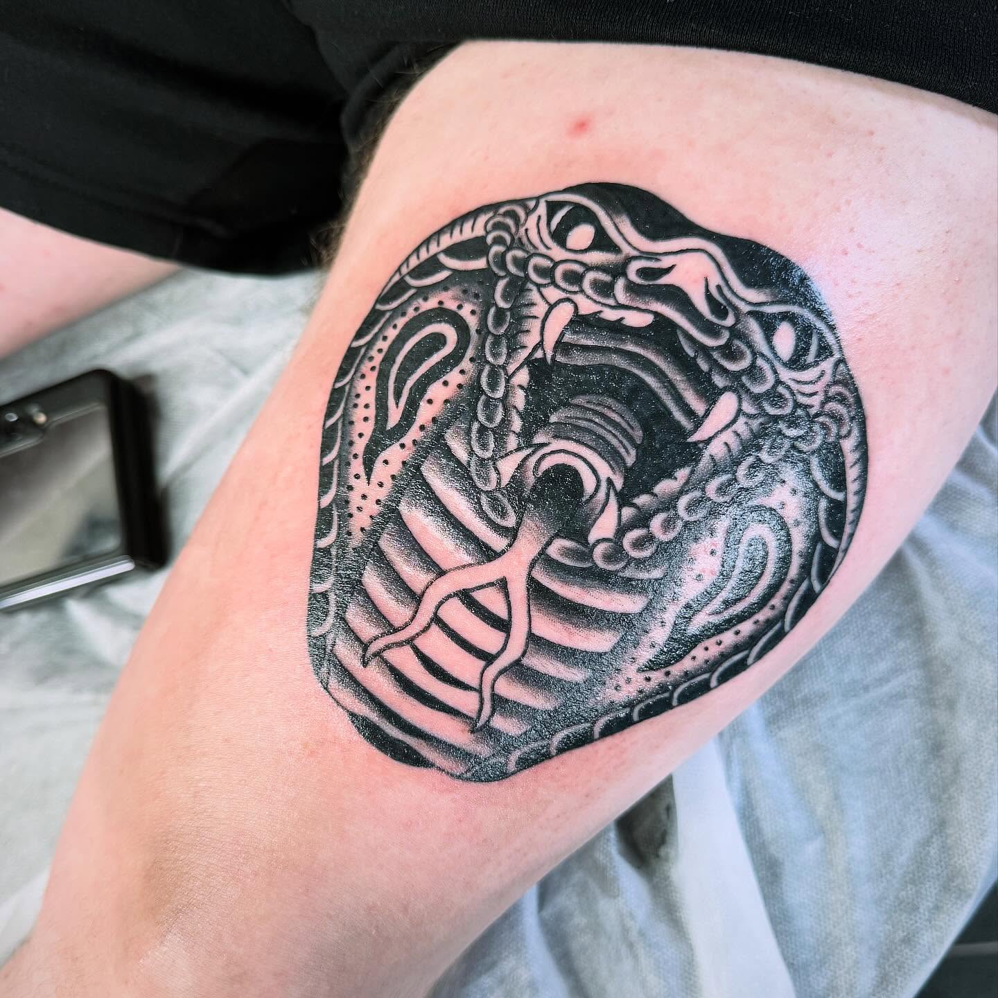 A snake coiled through a ribcage tattooed in bold black and grey on a thigh