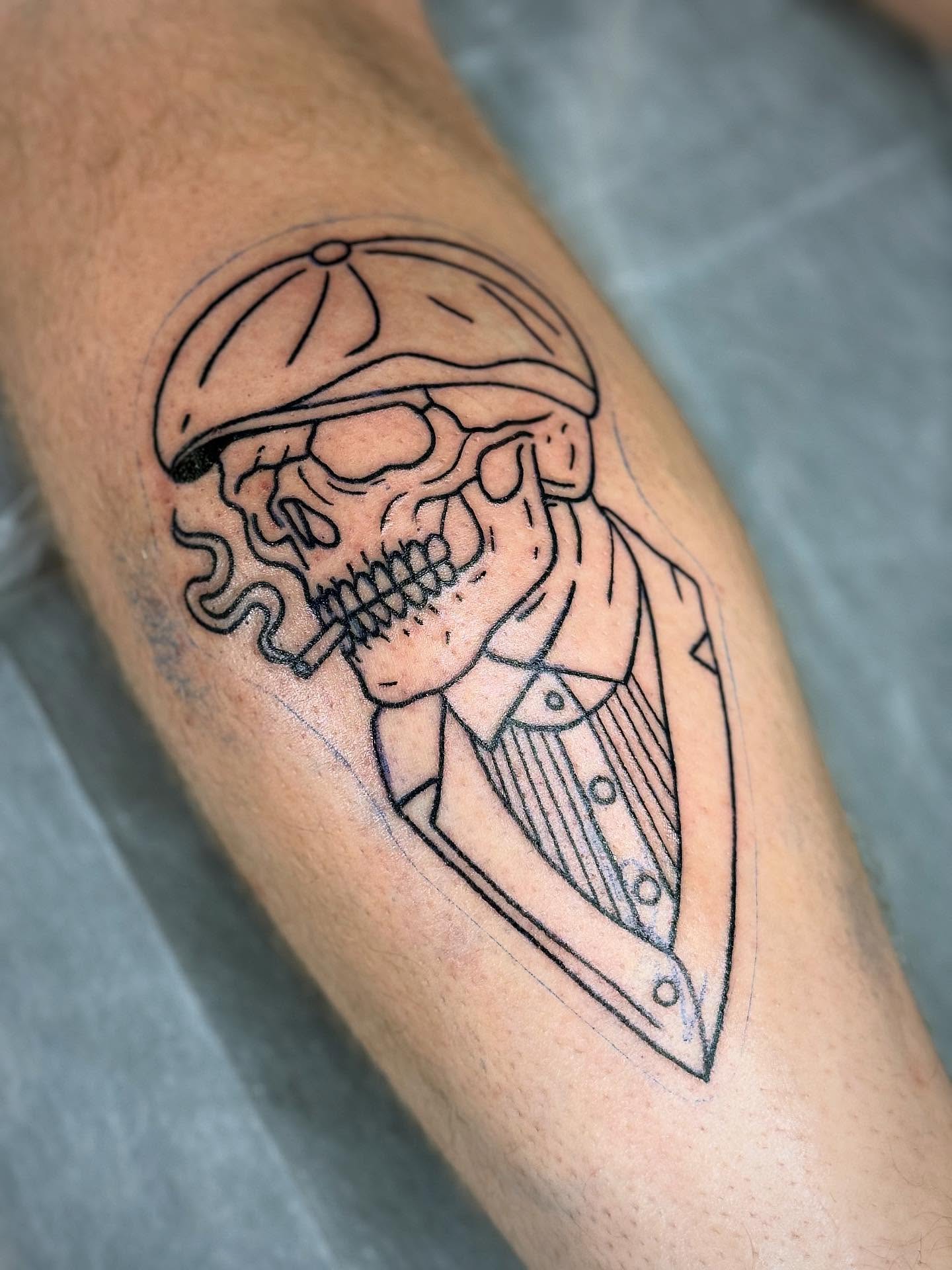 A skull wearing a flat cap and suit, tattooed in clean black outline