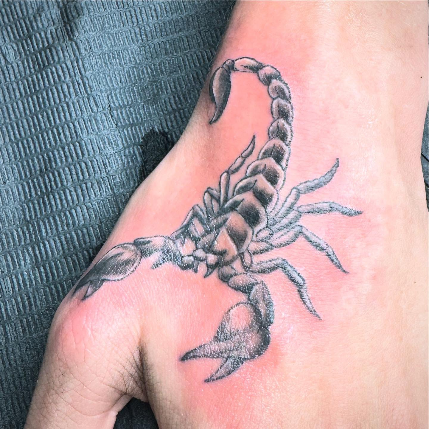 A scorpion tattooed in black and grey on the back of a hand