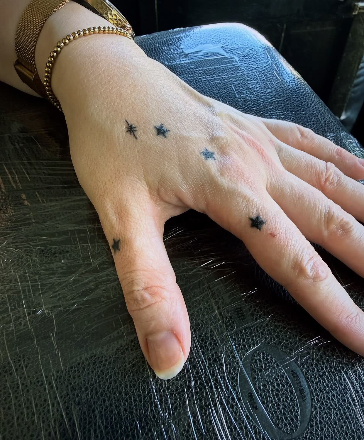 A scatter of small black star tattoos across the back of a hand